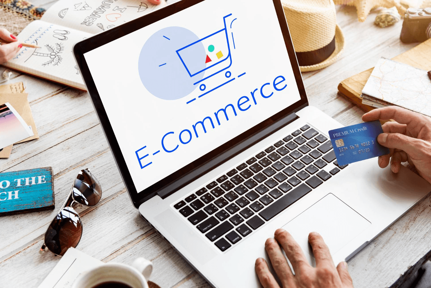 Notebook con la palabra E-Commerce en pantalla y una mano sosteniendo una tarjeta de crédito